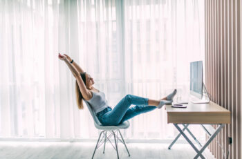 Young female freelancer stretching and relaxing working on laptop in home office